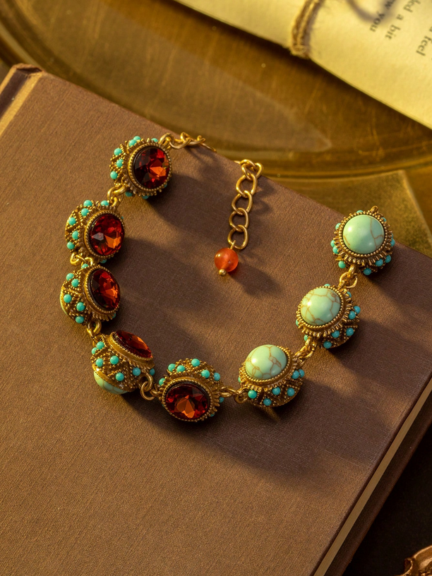 Gold bracelet with red and turquoise stones on a brown surface