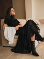 Woman in a black dress and boots sitting on a beige couch in a room with a neutral color palette.