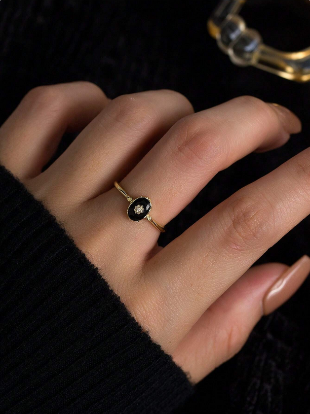 Gold ring with a black stone on a person's finger against a dark background