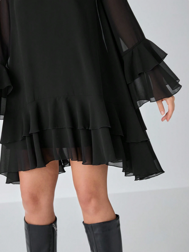 Black layered dress with sheer sleeves and ruffled skirt on a white background