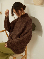 Woman wearing a brown sweater sitting on a chair in a minimalistic room.