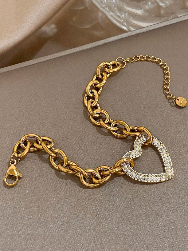 Gold chain bracelet with a heart-shaped diamond charm on a neutral background
