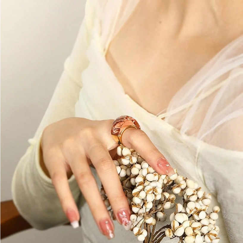 Close-up of a hand holding a branch with small white flowers, wearing a ring.