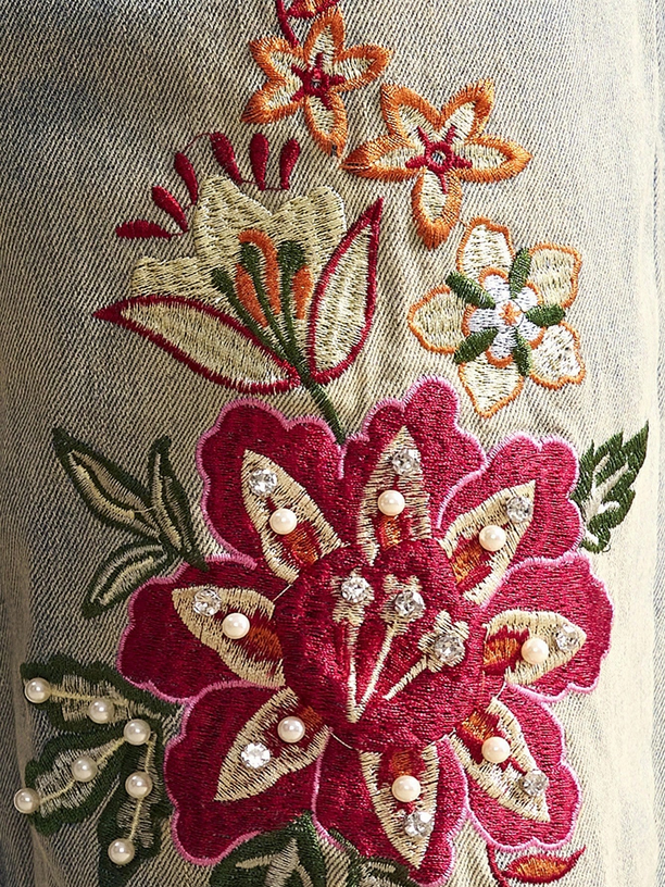 Close-up of embroidered floral design with red, gold, and green colors on a fabric background.