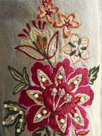 Close-up of embroidered floral design with red, gold, and green colors on a fabric background.