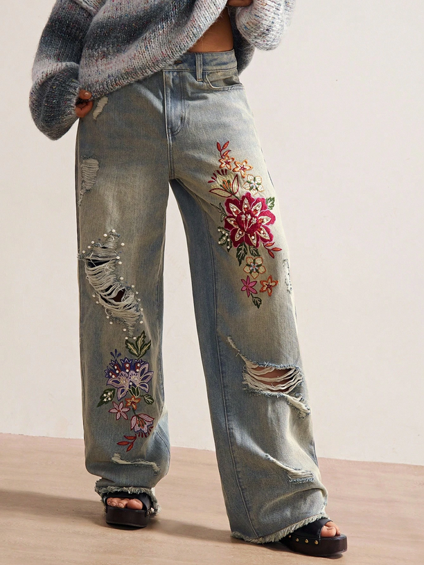 Distressed jeans with floral embroidery on a neutral background