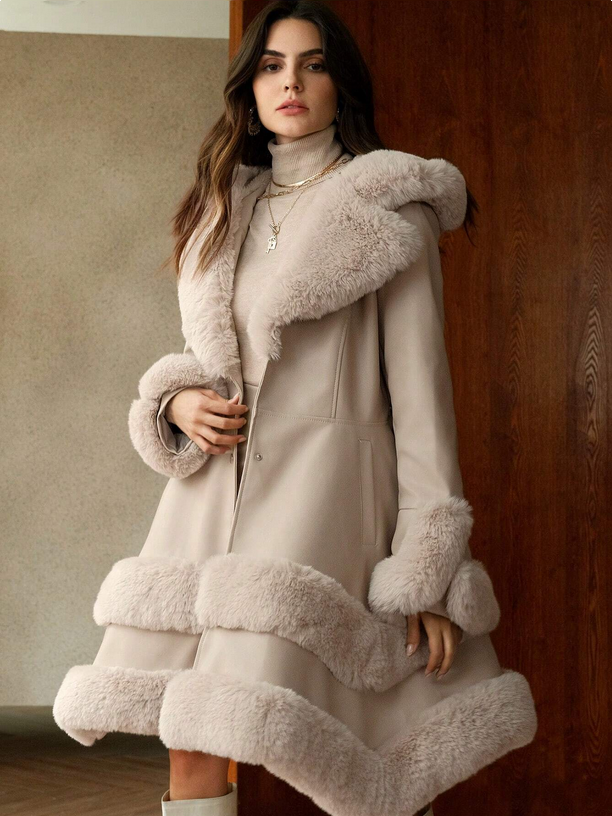 Woman wearing a long, light-colored coat with fur trim against a neutral background