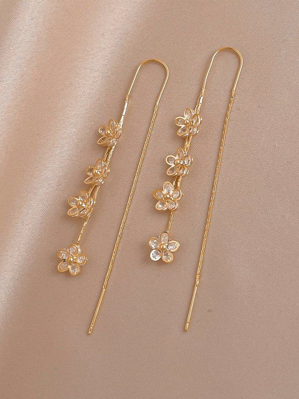 Gold floral earrings on a beige background