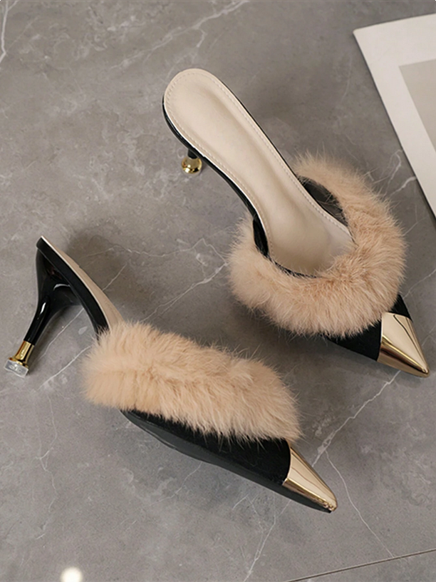 Black high-heeled shoes with beige fur on a gray marble surface