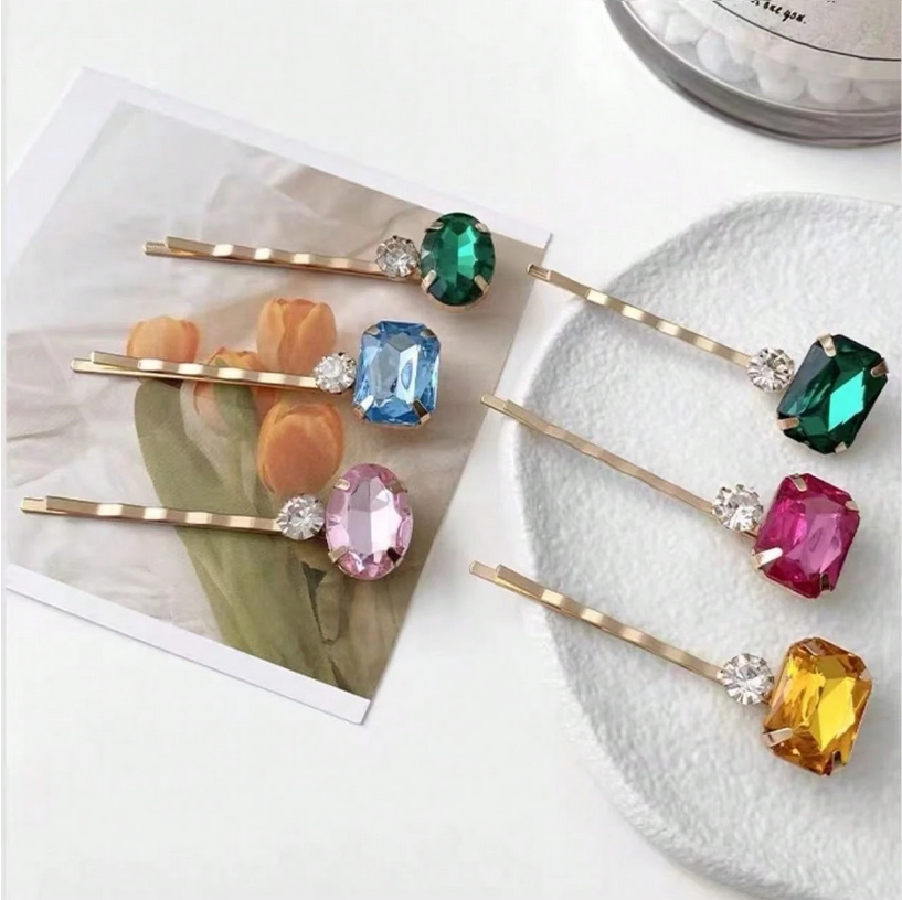 Set of colorful gemstone hair pins on a white surface with a magazine in the background.