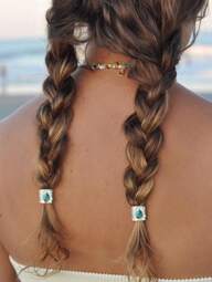 Back view of a person with braided hair adorned with decorative beads, against a blurred natural background.