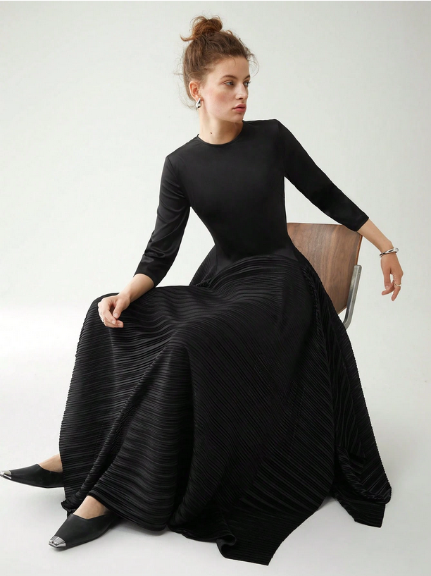 Woman wearing a black pleated dress sitting on a chair against a white background
