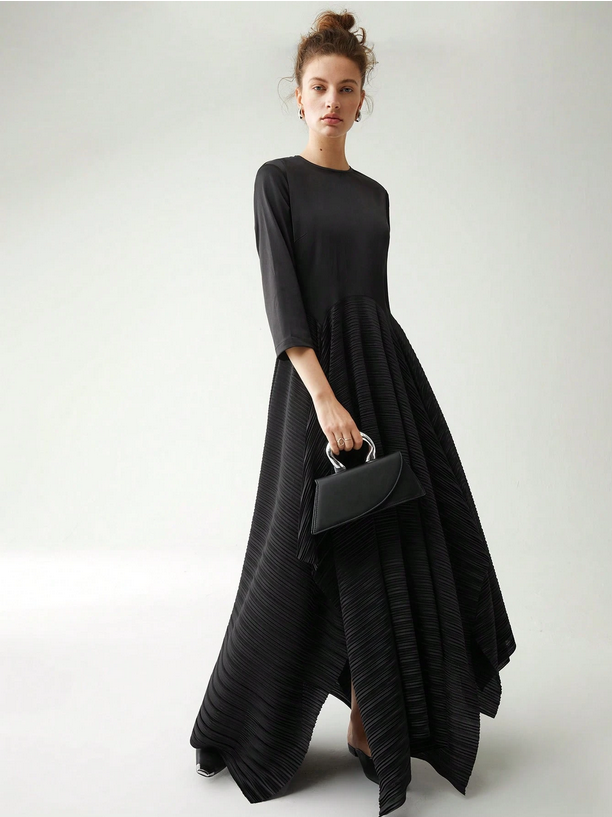 Woman wearing a black dress holding a matching handbag against a white background