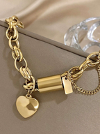 Gold chain bracelet with heart charm on a beige surface