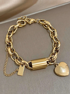Gold chain bracelet with cylindrical clasp and heart charm on a neutral background