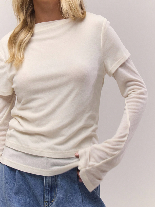 Person wearing a white long-sleeve top and blue jeans on a plain background