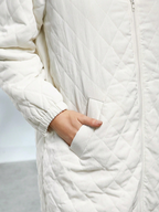 Close-up of a person wearing a white quilted jacket with a neutral background