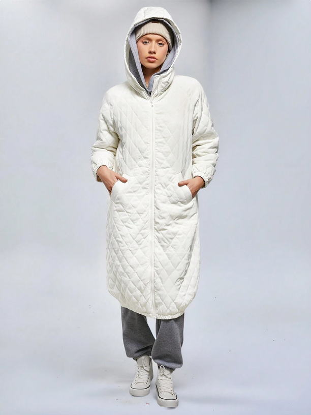Person wearing a long white quilted coat on a plain background