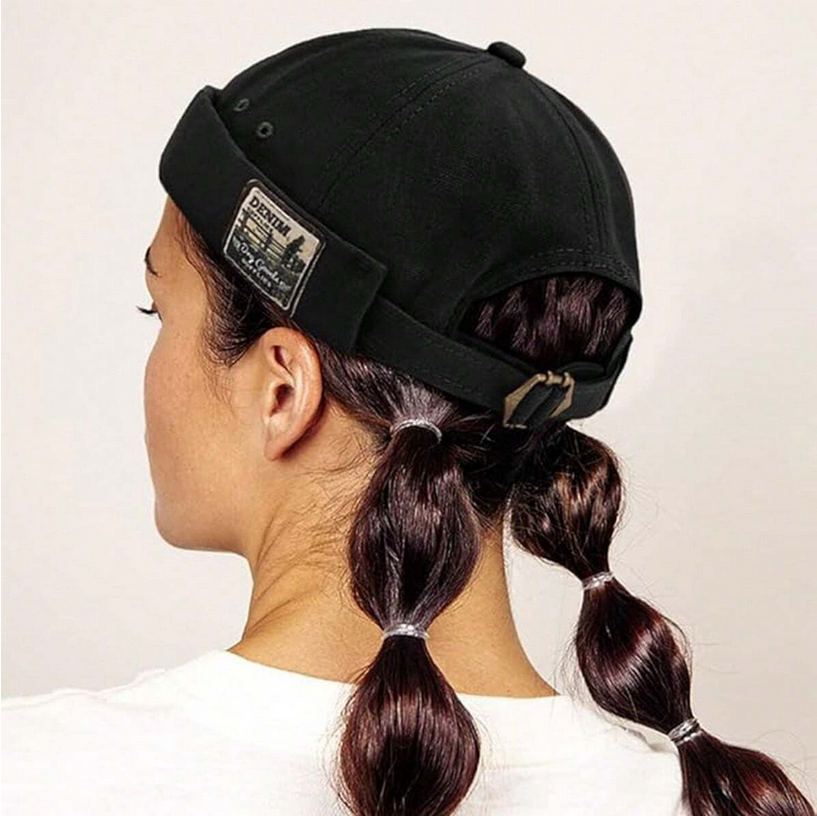 Person wearing a black cap with braided hair on a plain background