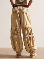Beige layered pants worn by a person on a neutral background