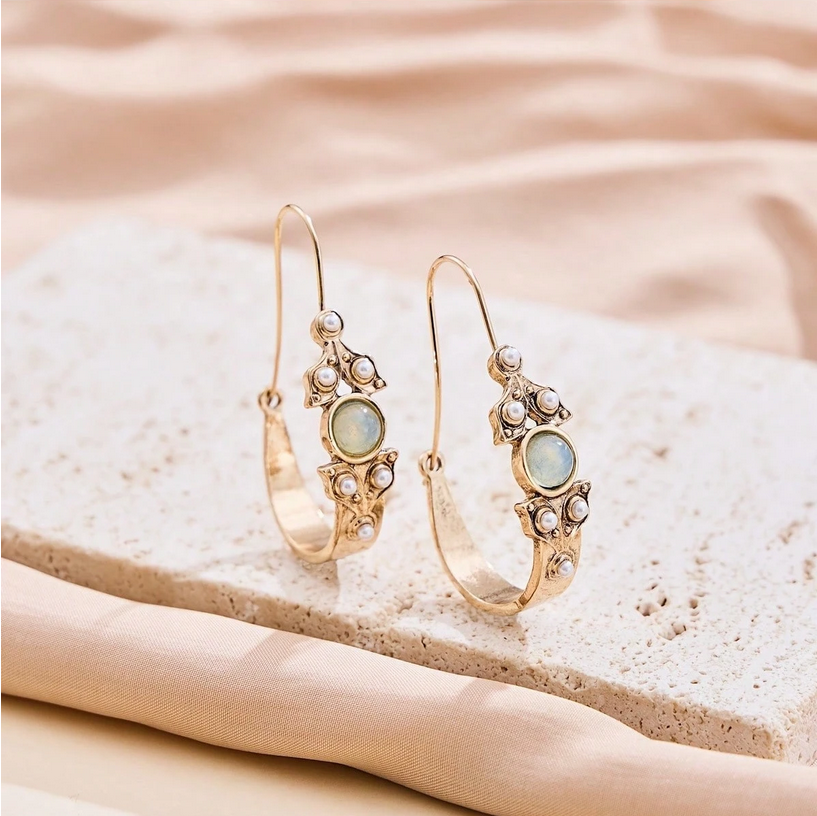 Gold hoop earrings with gemstones on a beige stone surface