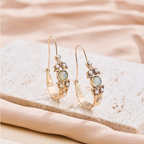 Gold hoop earrings with gemstones on a beige stone surface