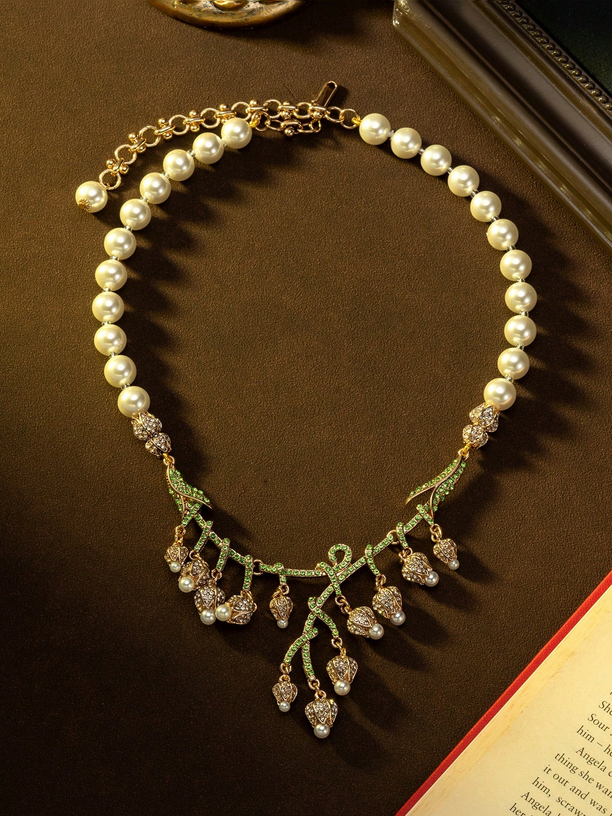 Pearl necklace with green leaves and crystal accents on a brown surface