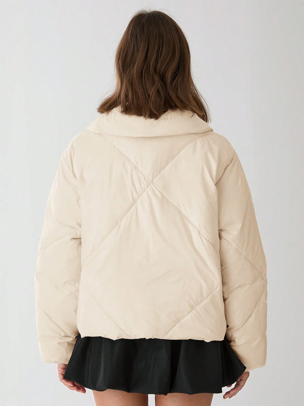 Person wearing a beige quilted jacket on a plain background