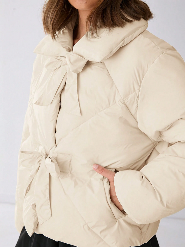 Beige puffer jacket with a bow detail on a plain background