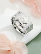 Silver ring with engraved design on a white surface with pink flowers