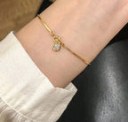 Gold bracelet with a small heart charm on a wrist against a neutral background