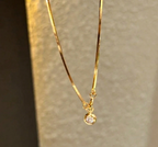 Gold necklace with a small pendant on a neutral background