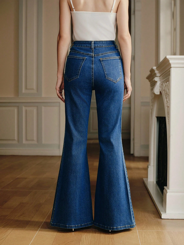 Person wearing blue flared jeans in a room with wooden floor and white walls.