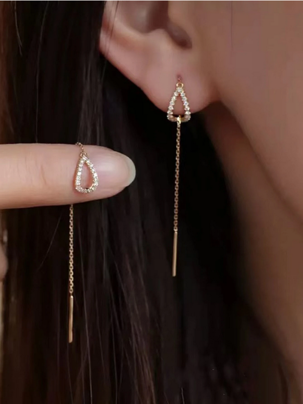 Gold earrings with chain details worn by a person, held up to the ear.