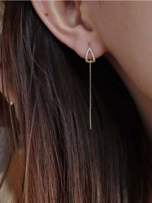 Close-up of an ear wearing a delicate gold earring with a chain
