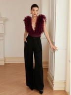 Woman wearing a burgundy feathered top and black pants in an elegant interior setting