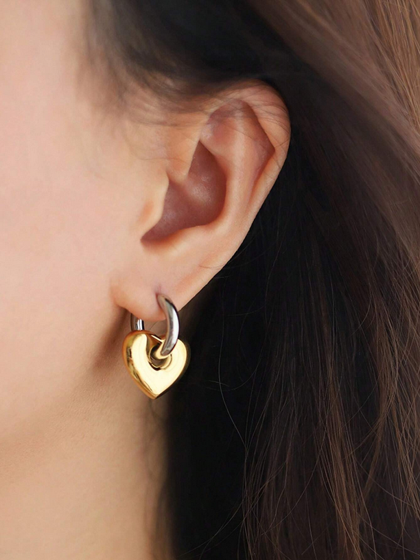 Gold heart-shaped earring worn by a person with dark hair.