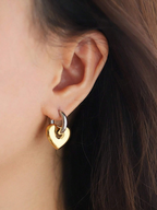 Gold heart-shaped earring worn by a person with dark hair.