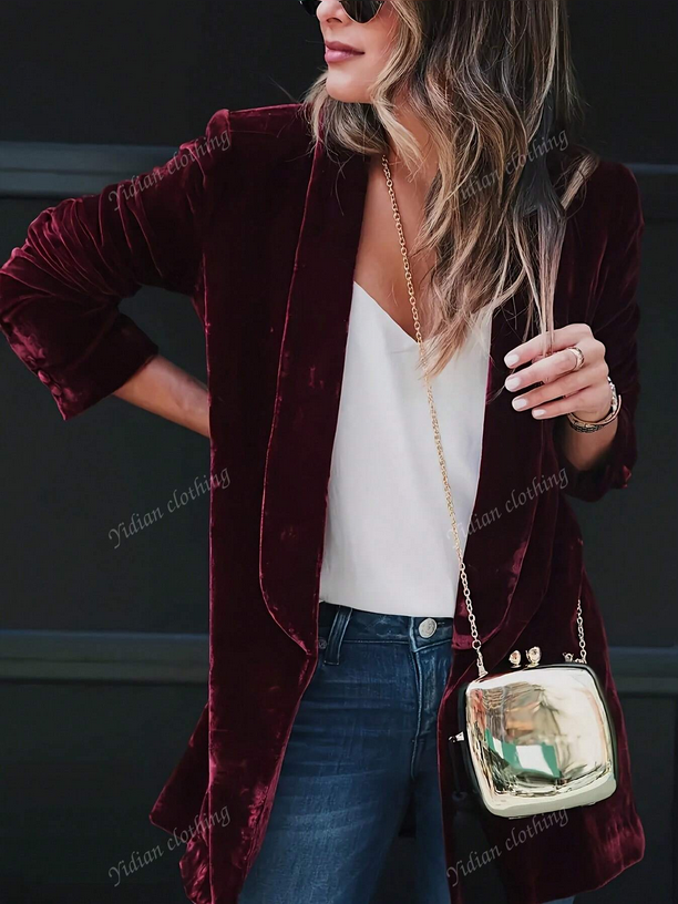 Woman wearing a burgundy velvet blazer over a white top and blue jeans, holding a small handbag.