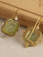 Gold earrings with green gemstones on a wooden surface
