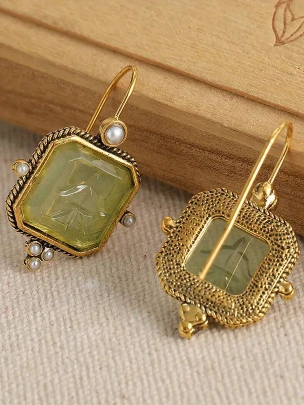 Gold earrings with green gemstones on a wooden surface