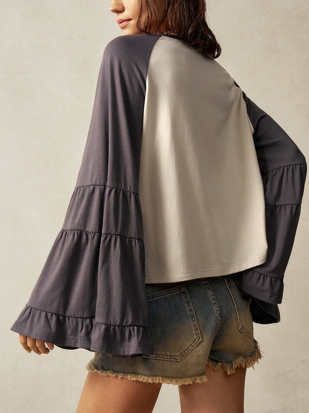 Person wearing a two-tone shirt with ruffled sleeves on a plain background