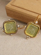 Pair of gold earrings with green gemstones and pearl accents on a beige fabric background.