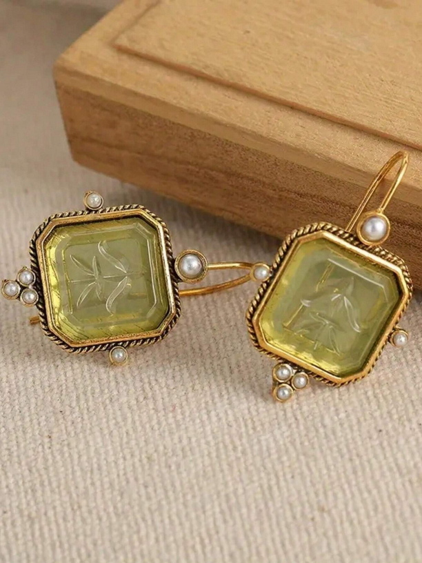 Pair of gold earrings with green gemstones and pearl accents on a beige fabric background.