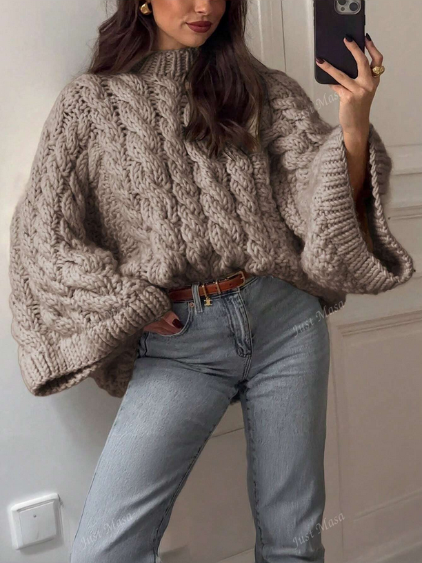 Person wearing a chunky knit sweater and light blue jeans, taking a mirror selfie.
